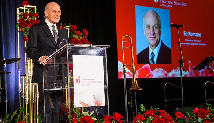 Ed Romano speaking from the podium with a photo of himself and the American Heart and Stroke Ball Los Angeles logo projected on a screen beside him.